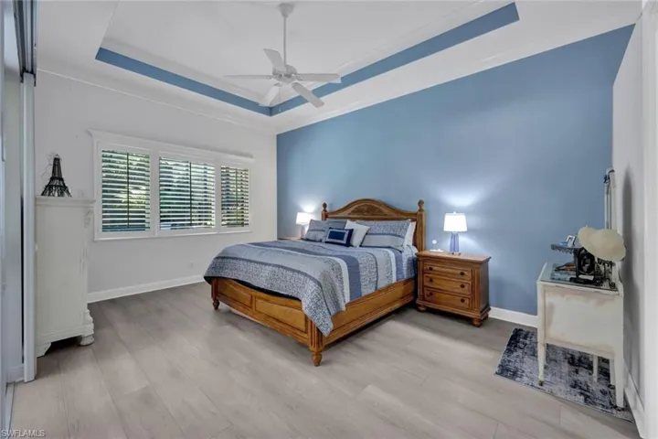 Bedroom with a raised ceiling, ceiling fan, new light vinyl planked flooring, and crown molding