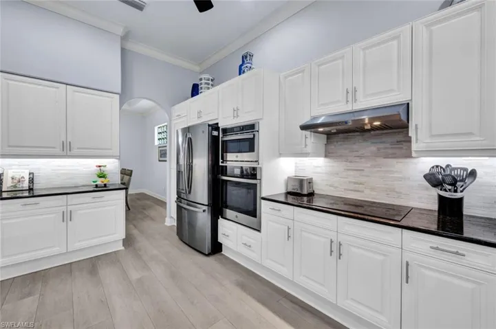 Kitchen featuring backsplash, ornamental molding, stainless steel appliances and white cabinetry