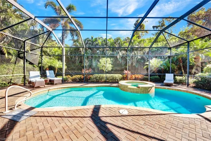 View of pool with connected hot tub, under screened-in lanai surrounded by lush landscaping offering a quiet preserve view.