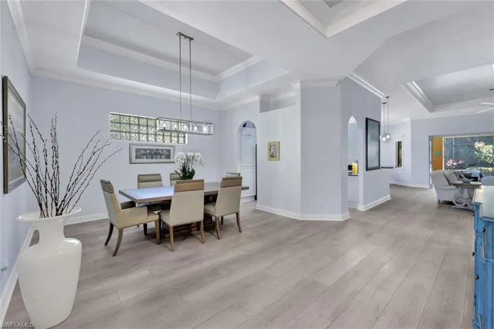 Dining area featuring a tray ceiling, new light vinyl planked flooring, arched walkways, and crown molding
