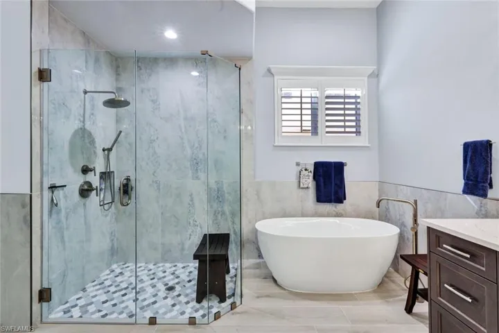 Full bathroom featuring tile walls, a freestanding tub, vanity, a stall shower, tile flooring and wainscoting