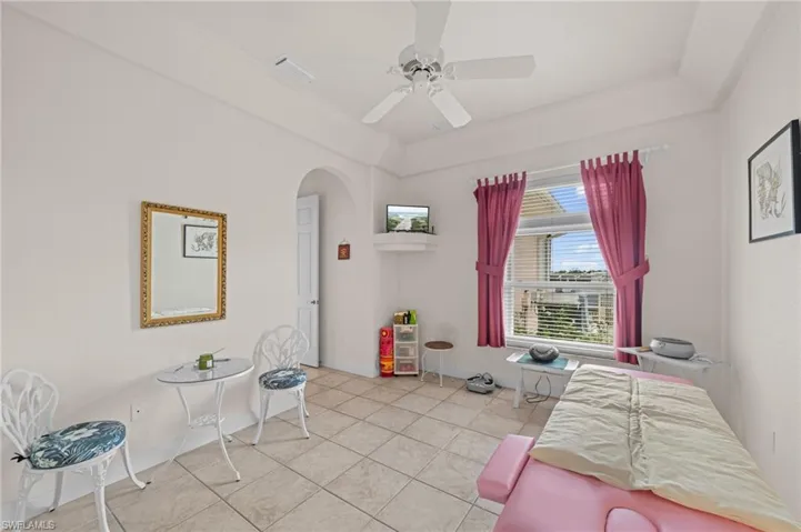 Bedroom featuring arched walkways, ceiling fan, a raised ceiling, and light tile patterned floors