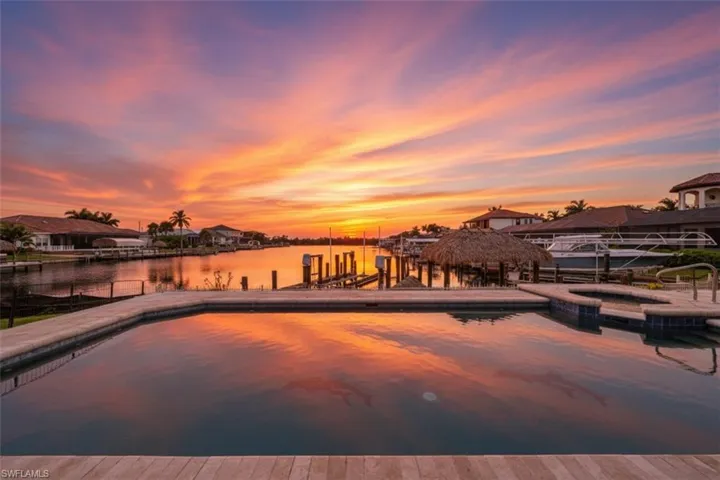 Pool at dusk with a water view, a pool with connected hot tub, and a boat dock