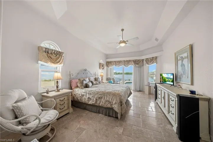 Bedroom with a raised ceiling, stone tile flooring, and ceiling fan