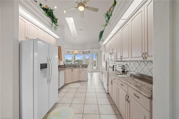 Kitchen with white appliances, a skylight, light tile patterned floors, pendant lighting, and dark stone counters