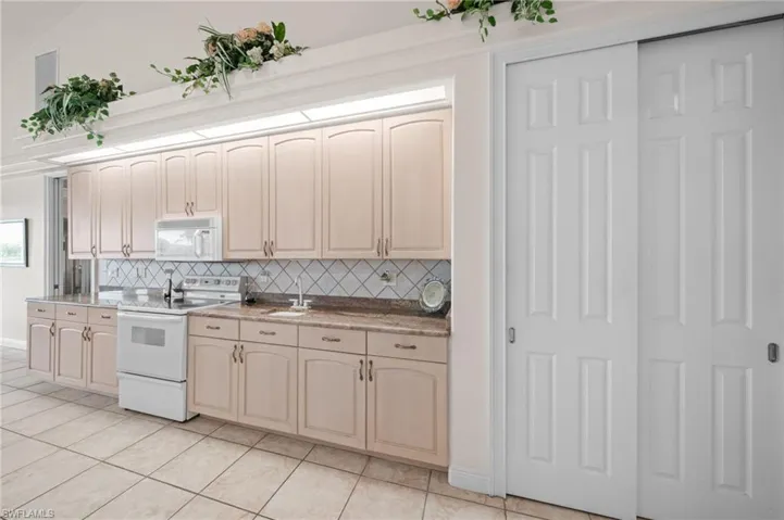 Kitchen with white appliances, tasteful backsplash, light tile patterned floors, and light stone counters