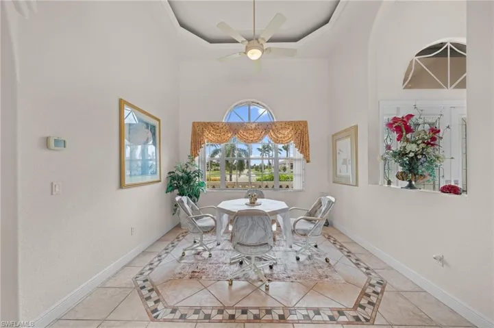 Dining room featuring inlaid floor details, light tile patterned floors, a towering ceiling, a ceiling fan, and a raised ceiling