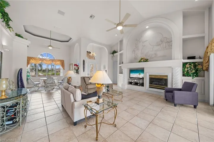 Living area with built in features, ceiling fan, a towering ceiling, arched walkways, and a glass covered fireplace