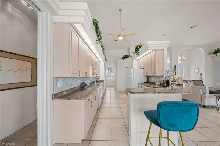 Kitchen featuring decorative backsplash, light tile patterned floors, white appliances, and dark stone countertops