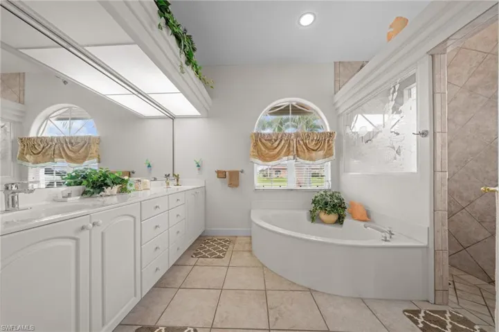 Full bathroom featuring a bath, double vanity, light tile patterned floors, and recessed lighting