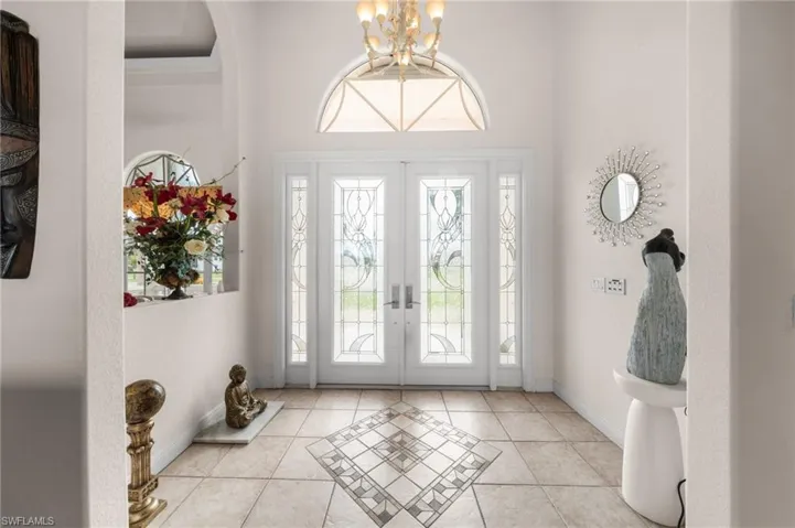 Foyer with light tile patterned flooring, french doors, inlaid floor details, and a chandelier
