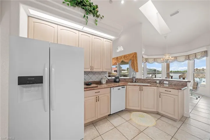Kitchen with white appliances, a chandelier, decorative backsplash, a skylight, and hanging light fixtures
