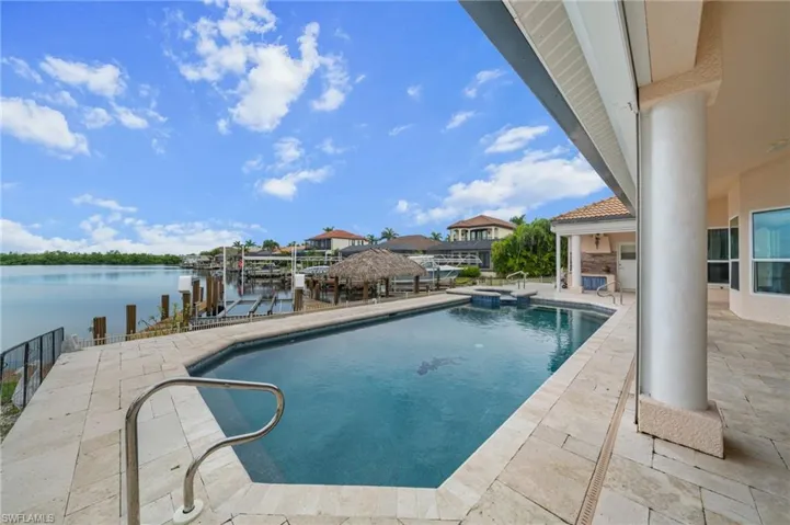 View of swimming pool featuring a patio area, a water view, a pool with connected hot tub, a boat dock, and boat lift
