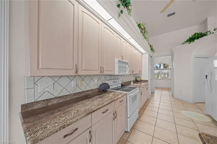 Kitchen with white appliances, decorative backsplash, light tile patterned floors, ceiling fan, and dark stone counters