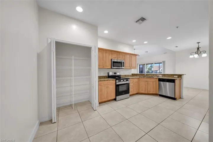 Kitchen with stainless steel appliances, a peninsula, light tile patterned flooring, recessed lighting, and decorative light fixtures