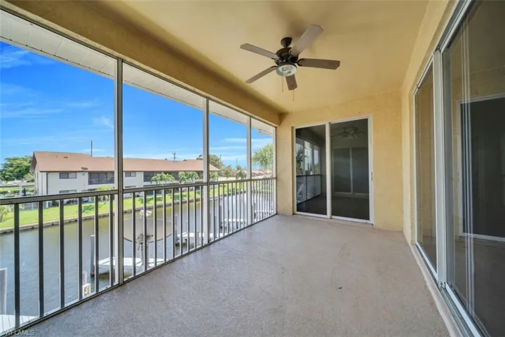 Unfurnished sunroom featuring a ceiling fan, a water view, and a balcony