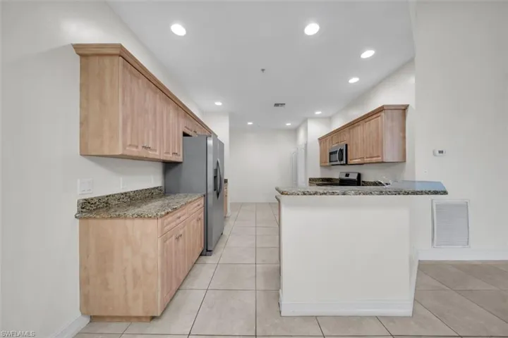 Kitchen featuring light brown cabinets, dark stone counters, a peninsula, light tile patterned floors, and recessed lighting