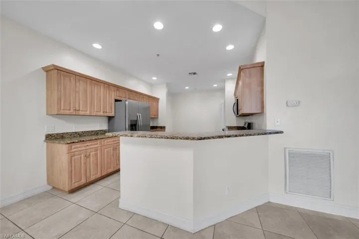 Kitchen with light brown cabinets, a peninsula, dark stone countertops, stainless steel refrigerator with ice dispenser, and recessed lighting