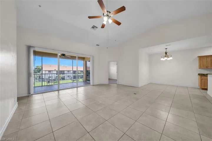 Unfurnished room with light tile patterned flooring, vaulted ceiling, a ceiling fan, and a chandelier