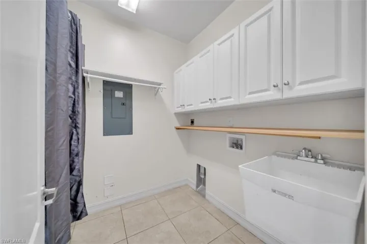 Laundry room with light tile patterned floors, electric panel, washer hookup, and cabinet space