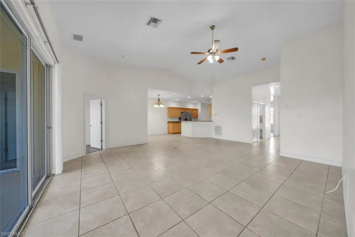 Unfurnished living room featuring lofted ceiling, light tile patterned floors, a ceiling fan, and a chandelier