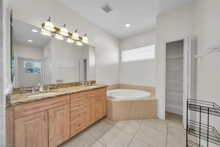 Full bathroom featuring double vanity, a bath, light tile patterned floors, and recessed lighting