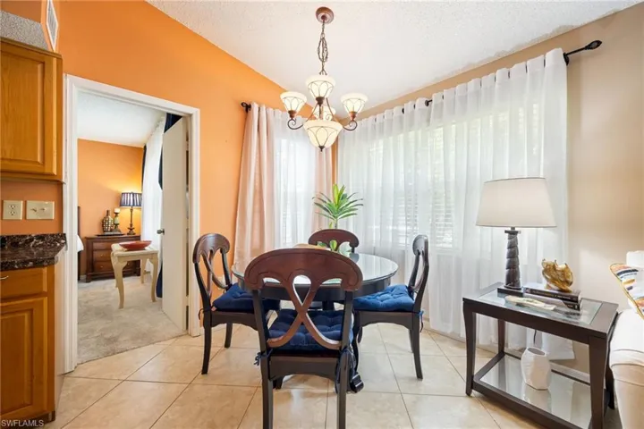 Dining area featuring tile flooring, a multi-light chandelier, a large window with sheer drapes, and an open doorway to an additional room