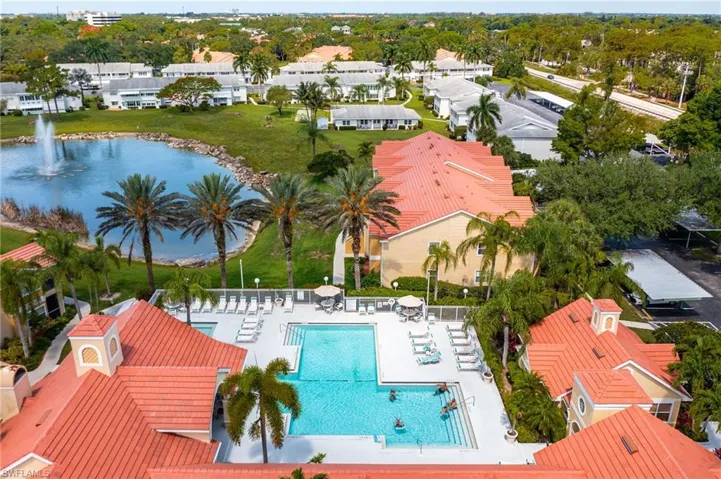 Community swimming pool with surrounding lounge deck, bordered by palm trees and buildings with red tile roofs
