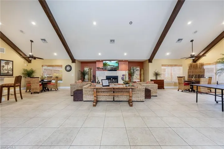 Spacious room featuring vaulted ceilings with exposed wood beams, recessed lighting, ceiling fans, and large format tile flooring