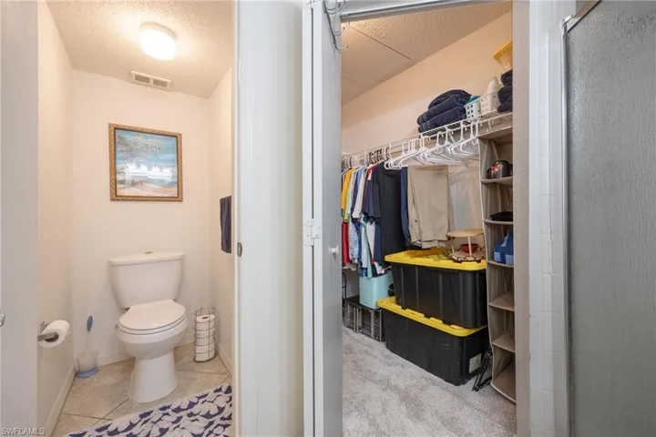 Powder room featuring tile flooring and an overhead light fixture, located beside a walk-in closet with carpet flooring and built-in wire shelving