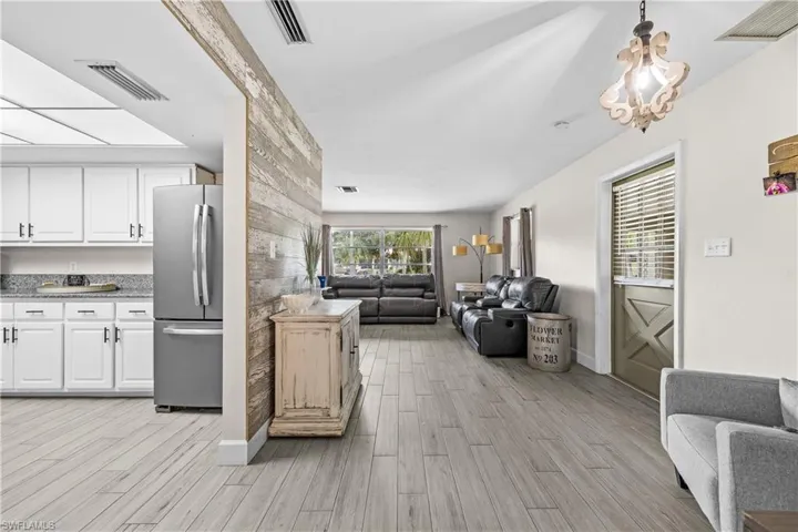 Open-concept interior featuring wood-finish tile flooring, a weathered wood-plank accent wall, vaulted ceilings, and a kitchen equipped with white cabinetry and stone countertops