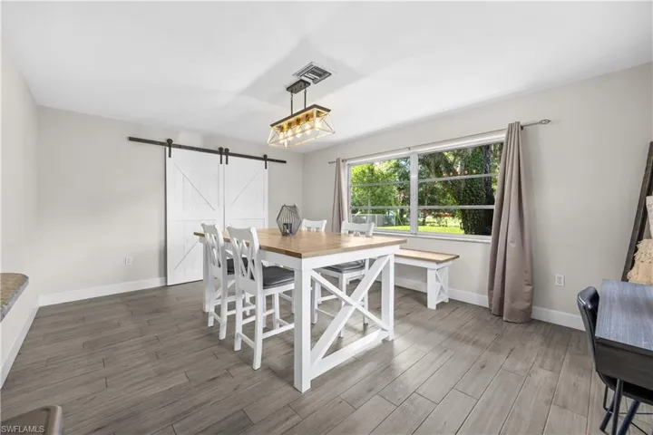 Room featuring wood-finish tile flooring, a sliding white barn door with black iron hardware, a rectangular window, and a multi-bulb linear pendant light fixture