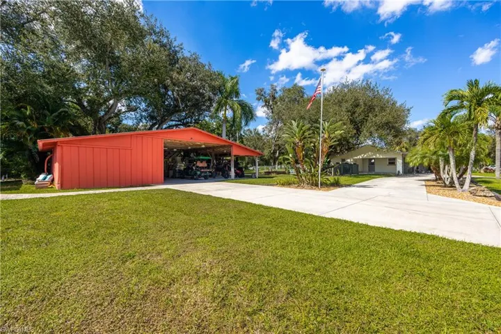 Expansive grounds featuring a metal-sided open-air outbuilding, a concrete driveway, mature landscaping, and established palm trees
