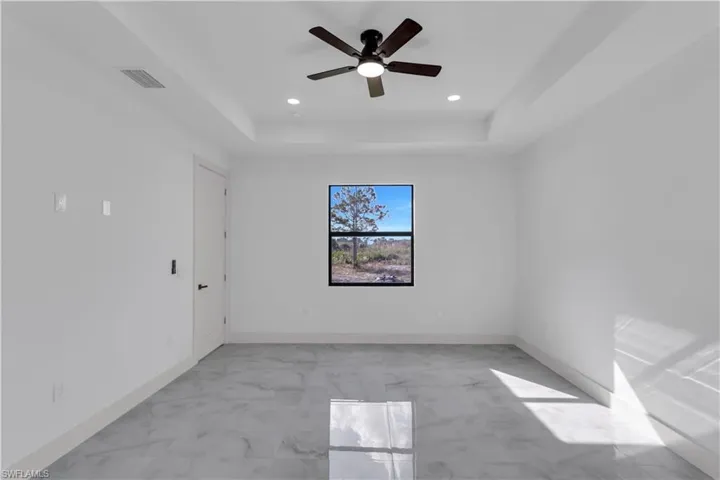 Spare room featuring a tray ceiling, light marble finish flooring, ceiling fan, and recessed lighting