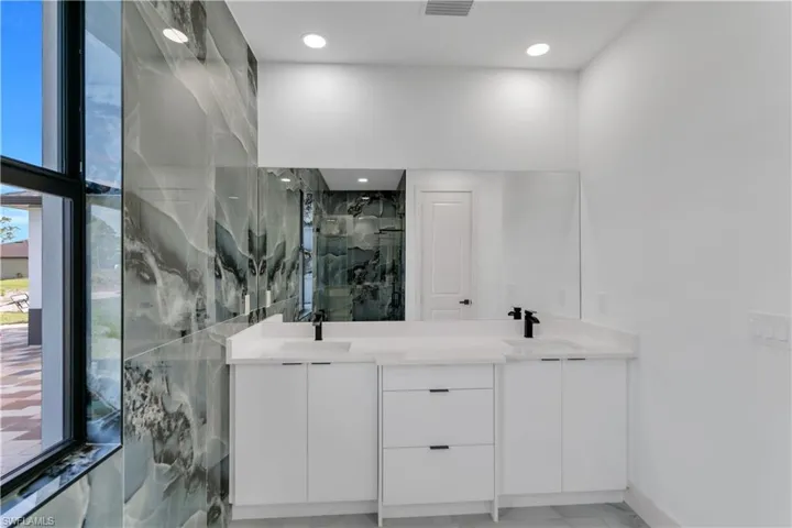 Bathroom with a marble finish shower, double vanity, and recessed lighting