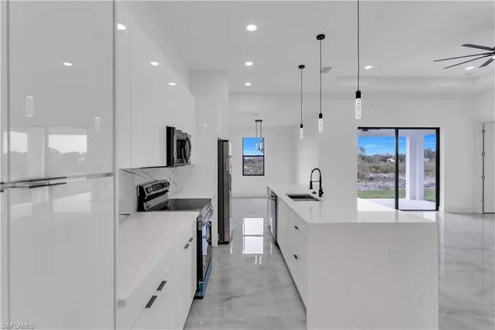 Kitchen with modern cabinets, stainless steel appliances, pendant lighting, white cabinetry, and light stone countertops