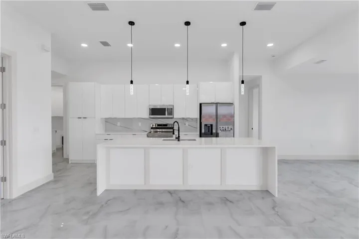 Kitchen featuring stainless steel appliances, white cabinetry, tasteful backsplash, a spacious island, and hanging light fixtures