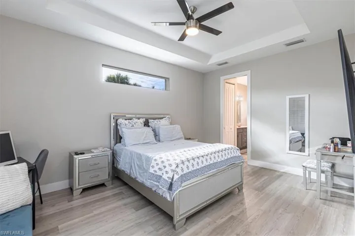 Bedroom featuring a raised ceiling, light wood-style floors, a ceiling fan, and ensuite bathroom