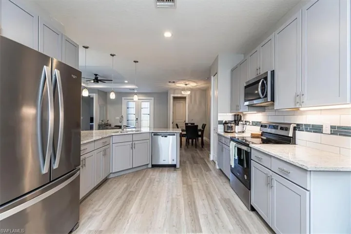 Kitchen with gray cabinets, appliances with stainless steel finishes, hanging light fixtures, light stone countertops, and recessed lighting