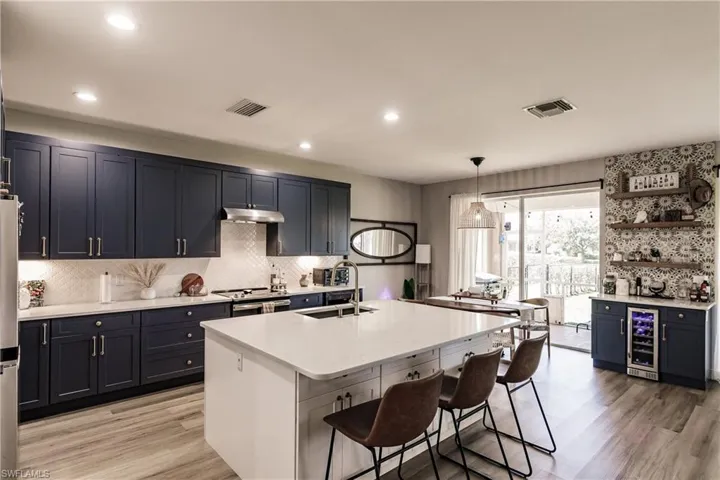 Kitchen with beverage cooler, light hardwood / wood-style floors, a kitchen island with sink, and backsplash
