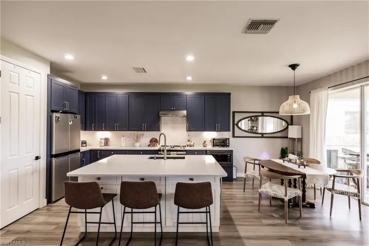 Kitchen with light hardwood / wood-style flooring, an island with sink, hanging light fixtures, sink, and stainless steel refrigerator