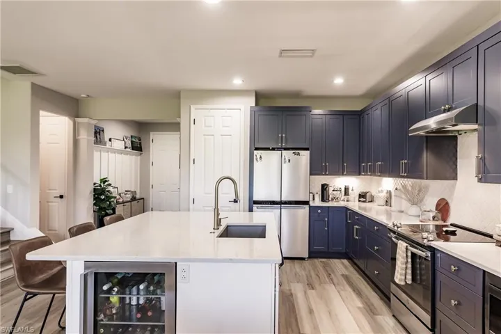 Kitchen featuring light hardwood / wood-style floors, beverage cooler, stainless steel appliances, a kitchen breakfast bar, and a center island with sink