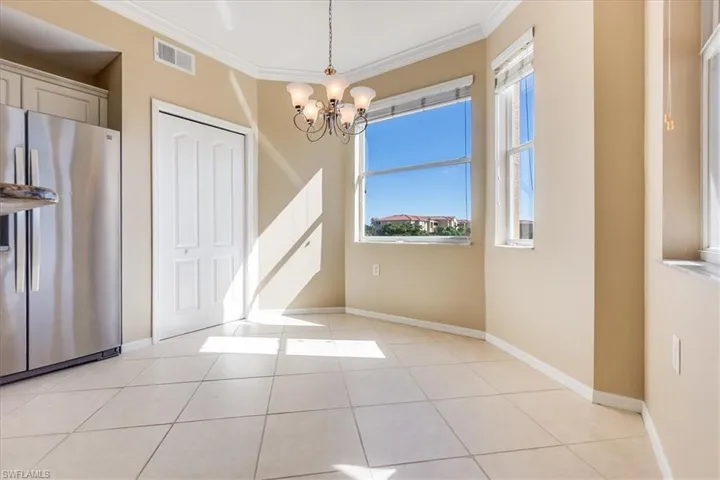 Bright and airy breakfast area with light tile patterned floors, ornamental molding, and an inviting chandelier.
