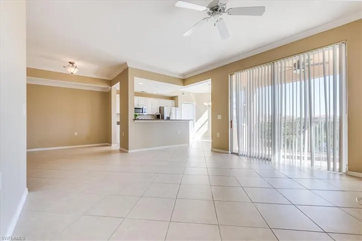 Unfurnished living room featuring light tile patterned floors, ceiling fan with notable chandelier, and ornamental molding.