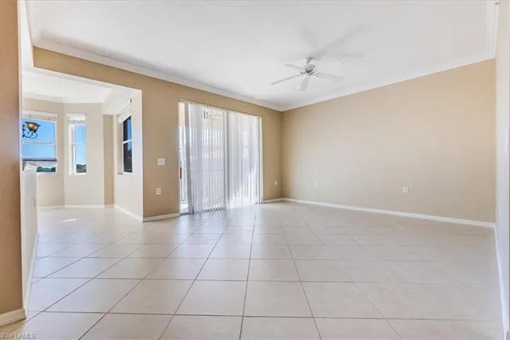 Living room with light tile patterned floors, ceiling fan, and crown molding.