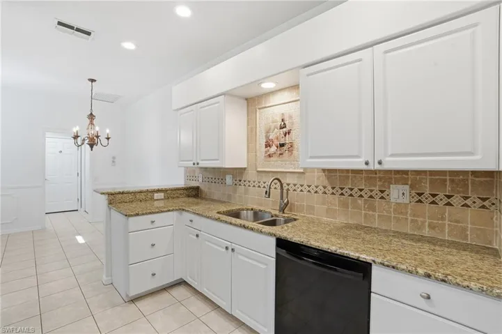Kitchen featuring black dishwasher, light stone countertops, white cabinets, light tile patterned floors, and pendant lighting