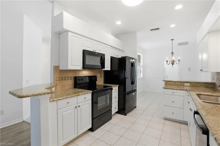 Kitchen featuring black appliances, light stone counters, pendant lighting, a peninsula, and white cabinetry