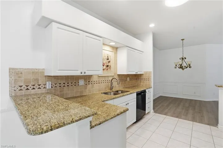 Kitchen with light tile patterned floors, hanging light fixtures, white cabinets, a chandelier, and light stone counters