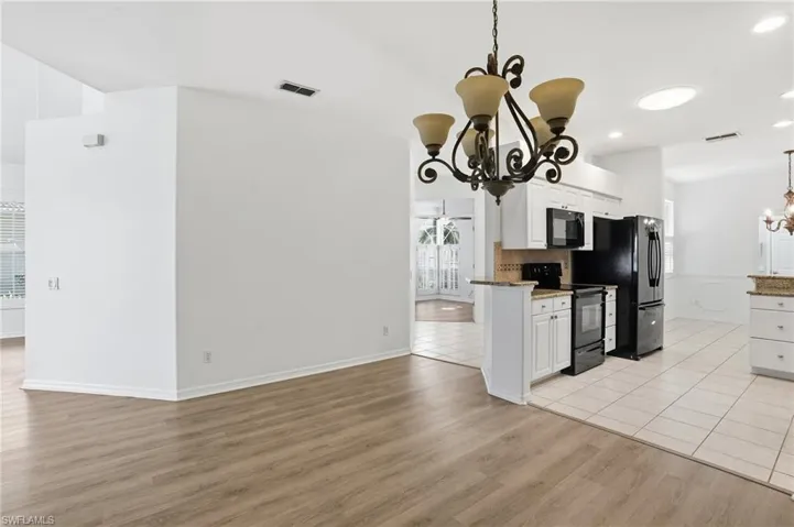 Kitchen with a chandelier, white cabinets, black appliances, light stone countertops, and hanging light fixtures