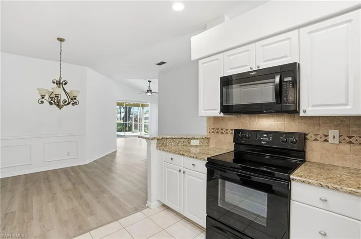 Kitchen featuring black appliances, white cabinetry, light stone countertops, decorative light fixtures, and a ceiling fan